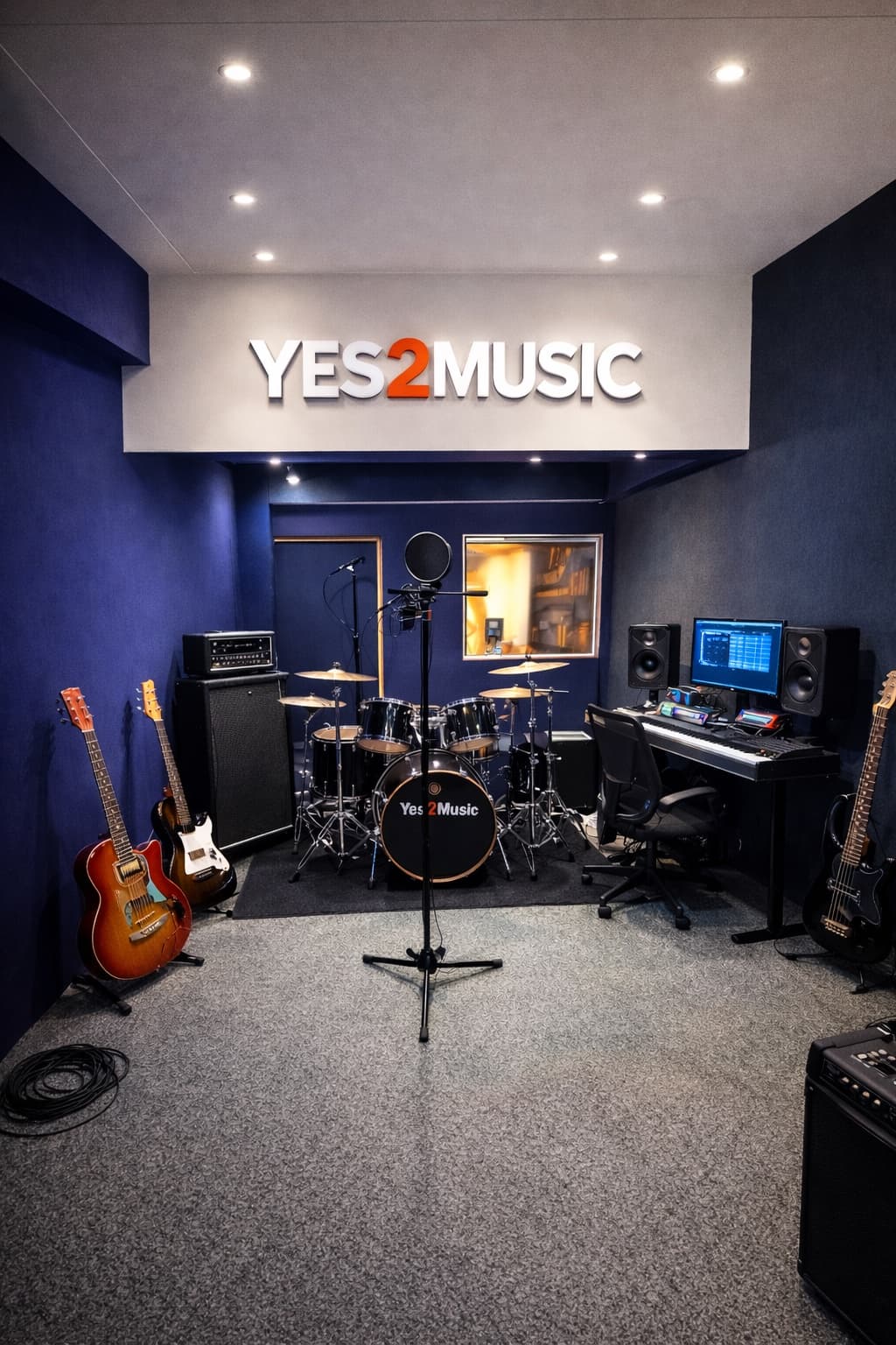 Yes2Music branded studio with drum kit, guitars, and control desk.